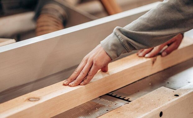 carpenter cutting wooden beam using table saw in workshop for custom millwork project