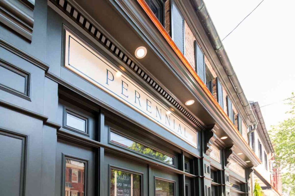 Exterior facade of Perennial, a restaurant or shop in a historic urban building, featuring a dark painted storefront with an illuminated sign and decorative molding.