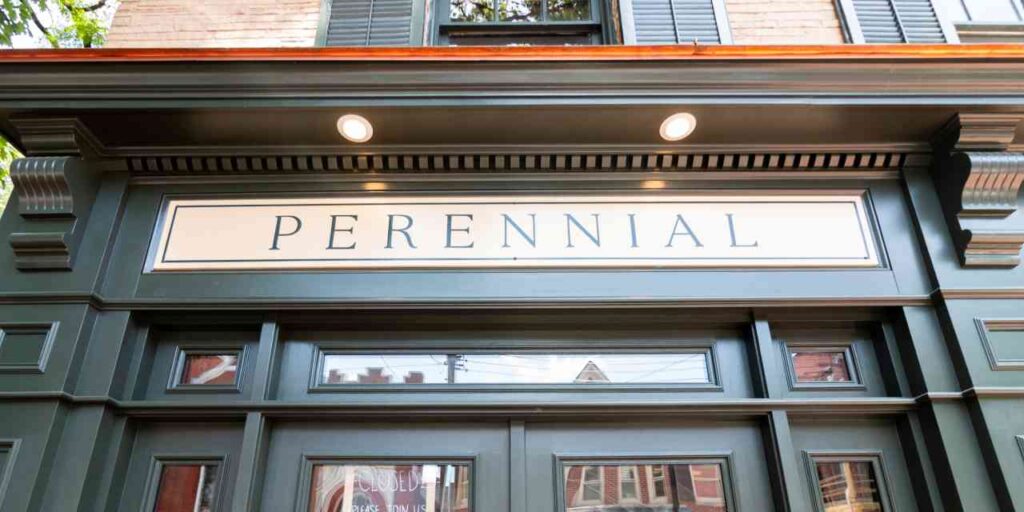 Close-up upward view of the Perennial storefront sign, framed by detailed architectural molding on a dark sage green painted facade.