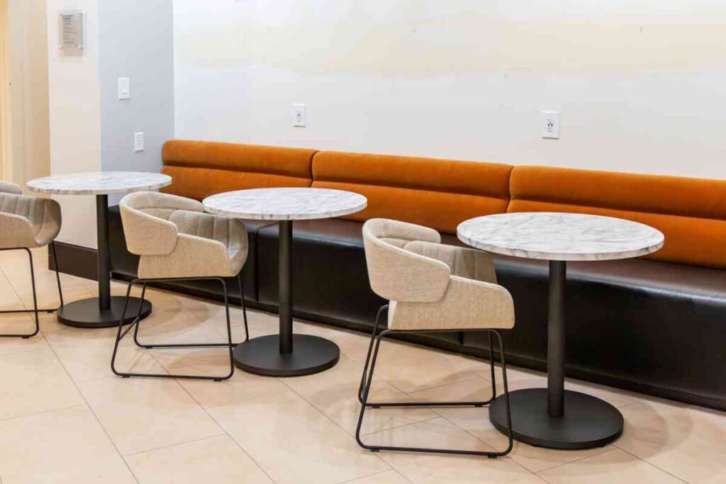A row of curved orange and black banquette seating paired with round marble-top bistro tables and cream upholstered chairs in a modern dining area.