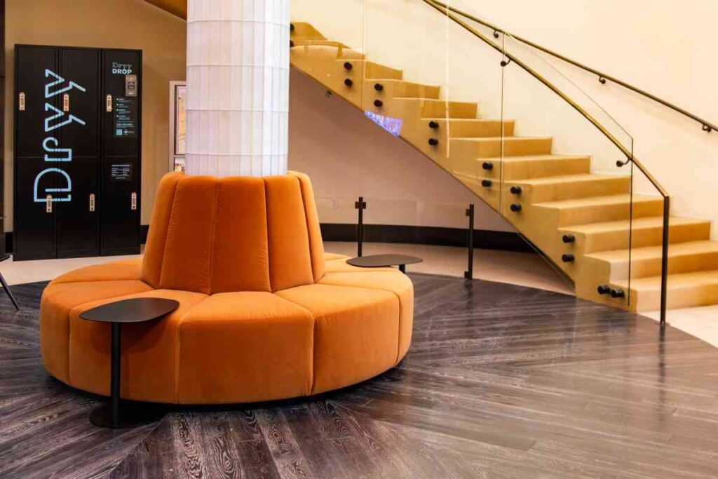 "A circular orange velvet sectional sofa with two small black side tables in a modern residential building lobby.