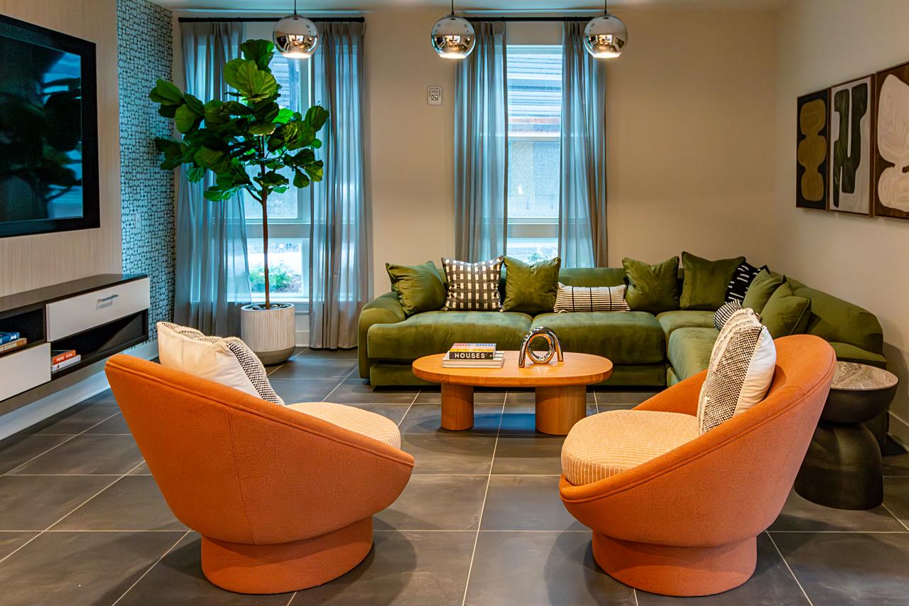Modern living room with two orange swivel chairs, a green sectional sofa, a wooden coffee table, potted plant, wall art, and large windows with sheer curtains.