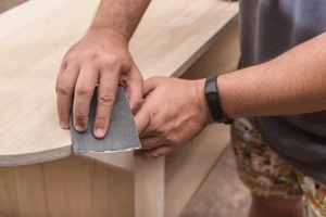 man uses a piece of sandpaper to smooth out the edge of a circular table