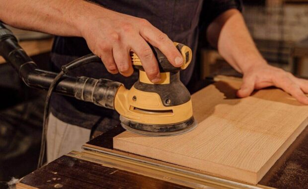 carpenter using an electric sander on a wooden board in a workshop