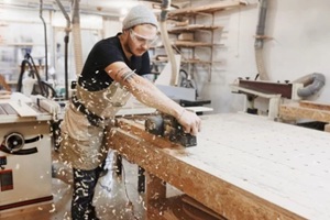 young carpenter using saw to cut wood pieces
