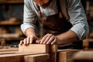 focused craftsman shapes a wooden block in a workshop filled with tools and timber